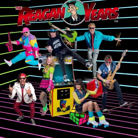 A group of seven people dressed in colorful 1980s-themed clothing pose energetically. They hold instruments such as a saxophone, guitar, and drums, with neon lights in the background and standing on a Pac-Man arcade machine and a Rubik's Cube.